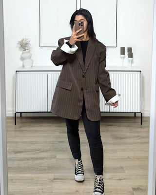 Blazer oversize marron à fines rayures blanches, coupe droite structurée avec épaules marquées, porté avec un jean noir et des baskets montantes.
