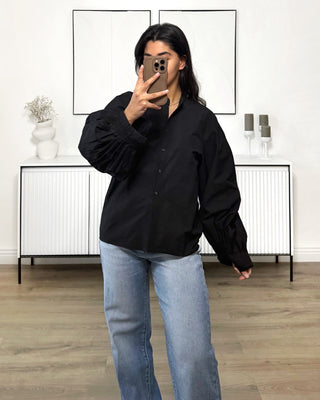 Chemise oversize noir à manches ballon, col classique et poignets boutonnés, portée avec un jean bleu.