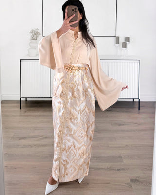 Caftan moderne deux pièces beige et doré composé d’un haut fluide à manches amples et d’une jupe longue brocart avec ceinture tressée.