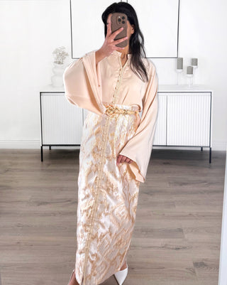 Caftan moderne deux pièces beige et doré composé d’un haut fluide à manches amples et d’une jupe longue brocart avec ceinture tressée.