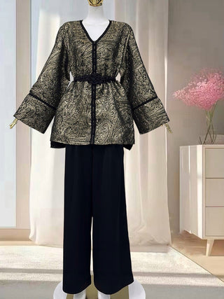 Veste kimono femme dorée et noire à motif brocart, coupe fluide avec manches larges et ceinture noire tressée, portée avec pantalon noir ample.