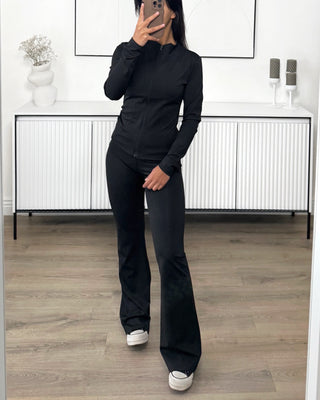 Ensemble de sport noir pour femme avec veste zippée ajustée et pantalon évasé en tissu stretch.