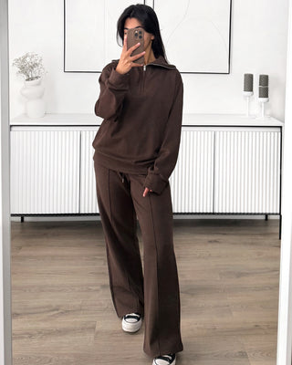Ensemble de survêtement marron composé d’un sweat à zip à col montant et d’un pantalon larges à taille élastique avec cordon de serrage, conçu dans un tissu doux et confortable. L’ensemble présente une coupe ample et décontractée, avec des lignes verticales discrètes sur le pantalon.