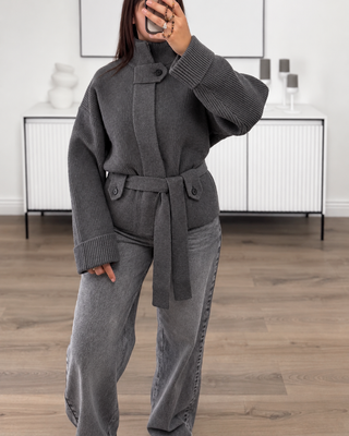 Gilet en maille gris côtelée à col montant, manches oversize et ceinture, porté avec un jean gris.