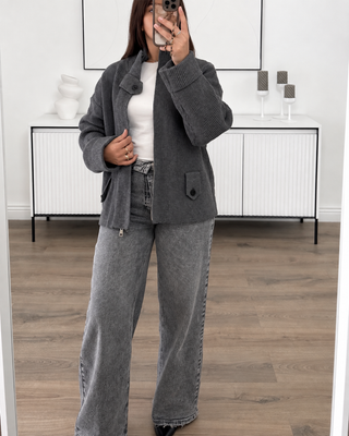 Gilet en maille gris côtelée à col montant, manches oversize et ceinture, porté avec un jean gris.