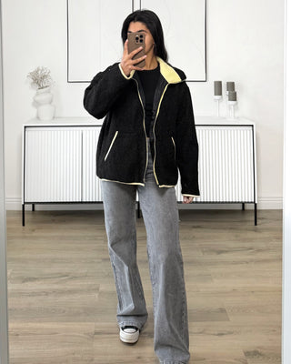 Jean en denim gris clair à taille haute et coupe droite, porté par une femme avec une veste noire à manches longues, vue de face.