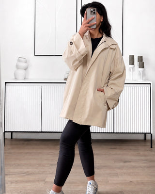 Trench mi-long mastour couleur beige. Coupe oversize pour femme, avec col montant, fermeture zippée et manches longues.