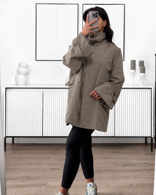 Trench mi-long mastour couleur taupe. Coupe oversize pour femme, avec col montant, fermeture zippée et manches longues.